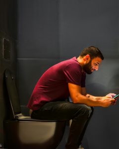 Mann beim Stuhlgang auf Toilette mit Smartphone